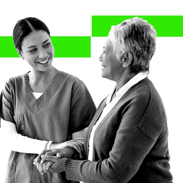 Young female healthcare professional smiles as she speaks to an older female patient and leads her by the arm