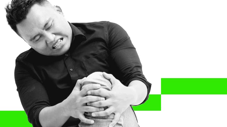 Asian man in his 30s wearing a dark shirt clutches his knee and grimaces in pain