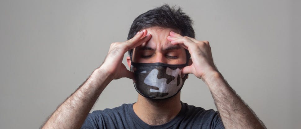 A man wearing a face mask & holding his forehead by both of his hands due to headache
