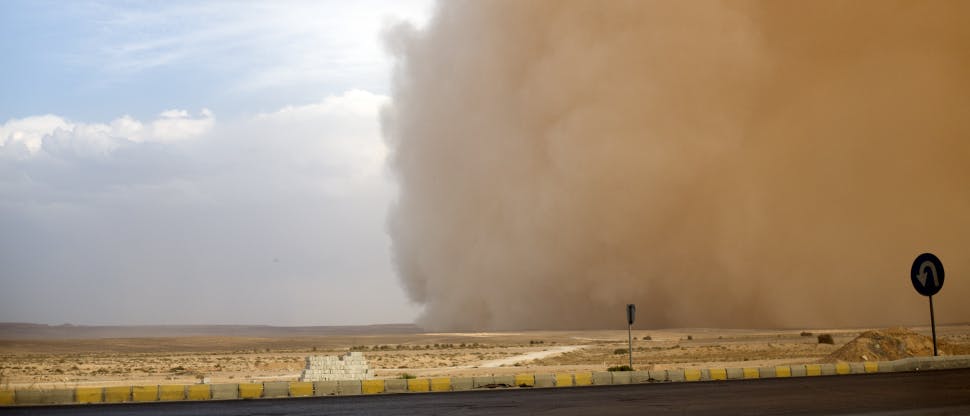 Image of a dust storm over a road and desert plain. The dust cloud takes over half of the sky