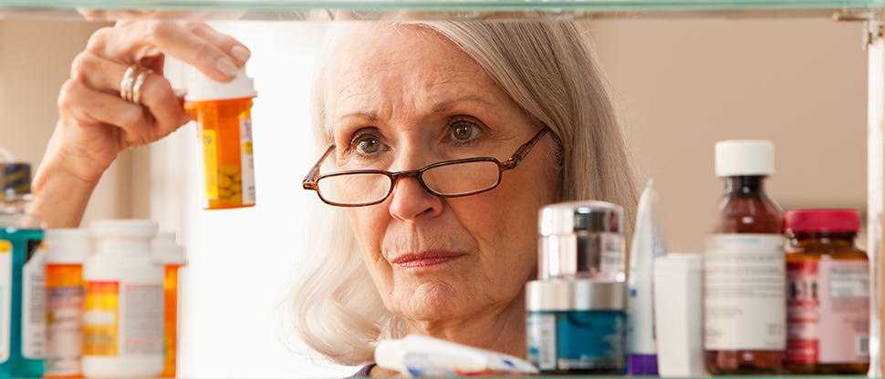 An older blonde woman wearing glasses inspects medicines in a medicine cabinet.