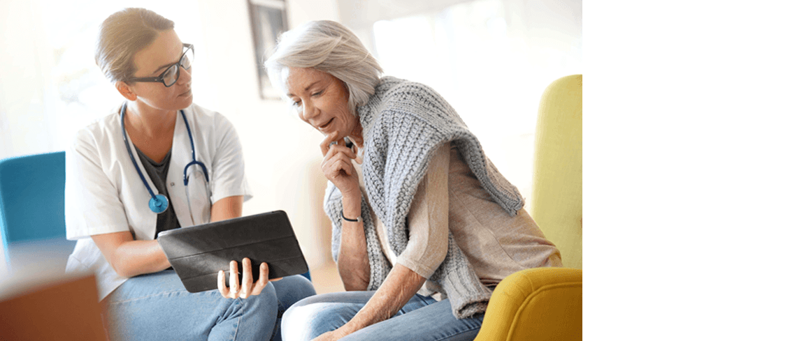 A doctor wearing a stethoscope around her neck and showing something to an older lady on a tablet 