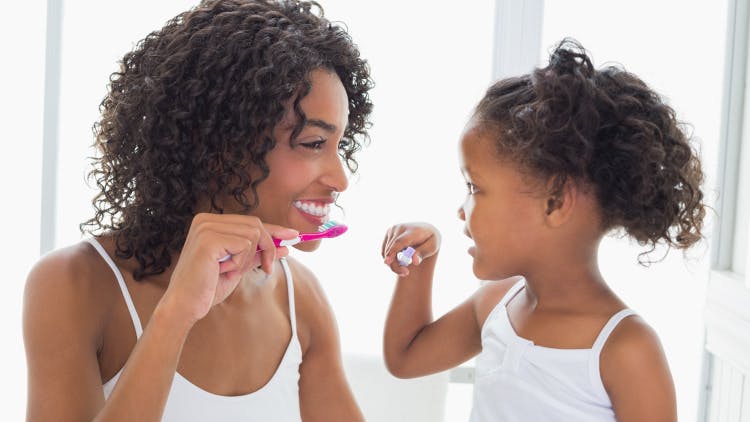 A mother and daughter happily brush their teeth together with a fluoride and sodium bicarbonate daily toothpaste.