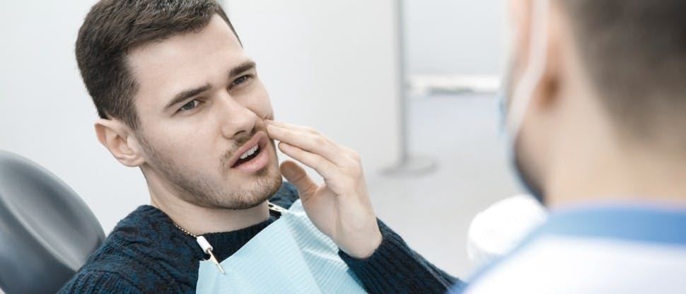 Man in dentist chair touching his jaw