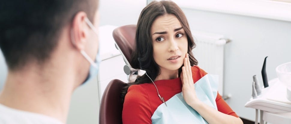 Woman in dentist chair touching her jaw
