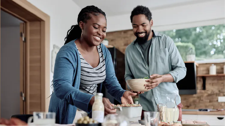 Two people preparing food together in a kitchen, standing at a counter with various ingredients and dishes.