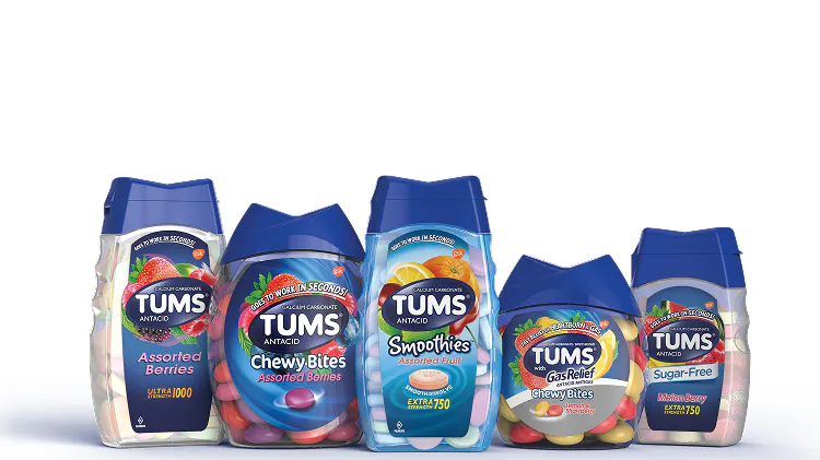 A group of five different TUMS antacid products. All containers have blue lids and various brightly colored tablets visible inside