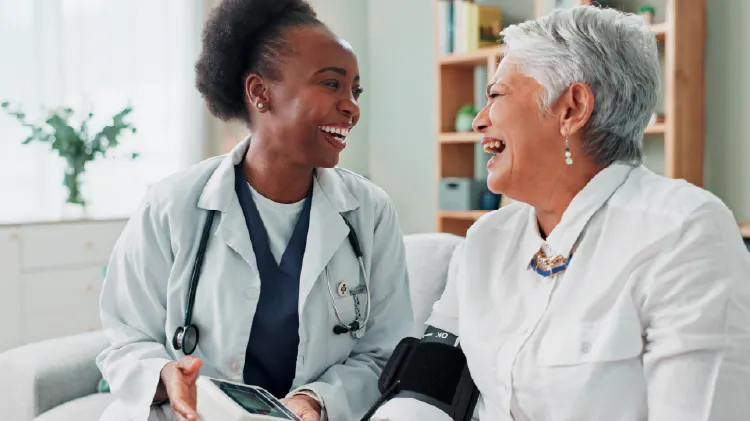 A doctor and a person in a medical office, talking and smiling at each other.