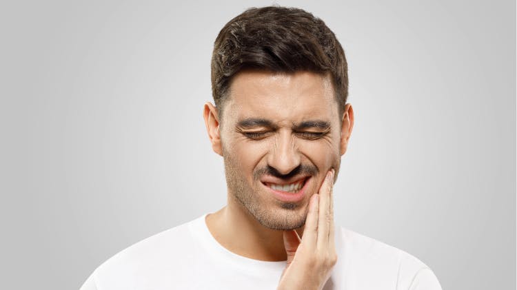 Man grimacing in pain and holding his hand to his face due to dentin hypersensitivity.