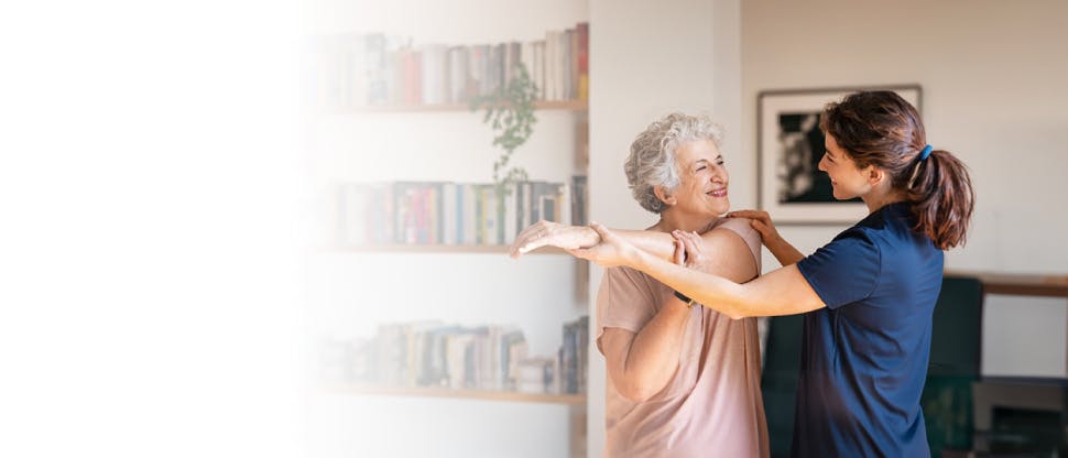 Happy senior woman doing exercise at home with physiotherapist.