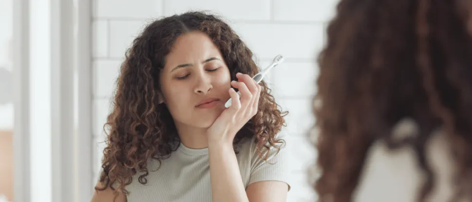 Woman holding a toothbrush and touching their cheek in pain