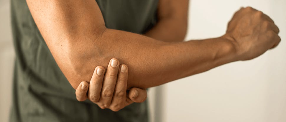 A man clutching his elbow as a result of pain from tennis elbow.