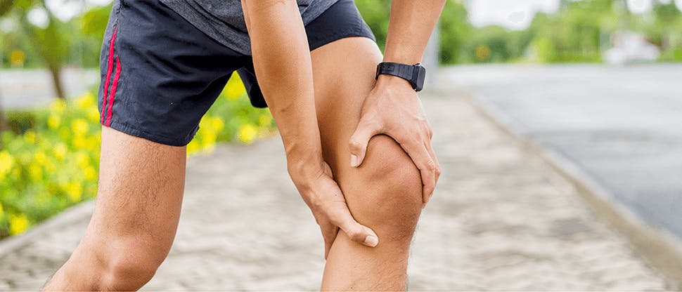 Image of a man outside in running attire clutching his knee as a result of bursitis pain