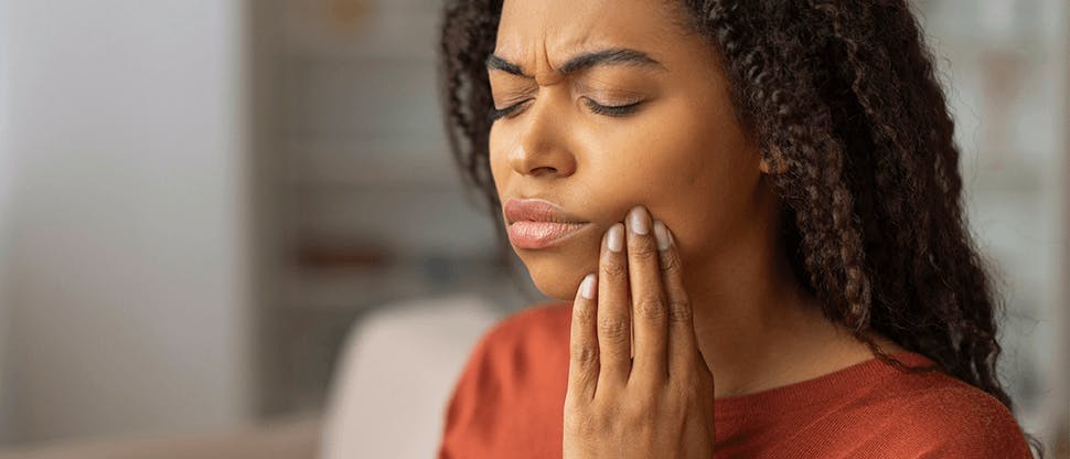 A woman clutching her face at the site of tooth pain in her lower jaw.