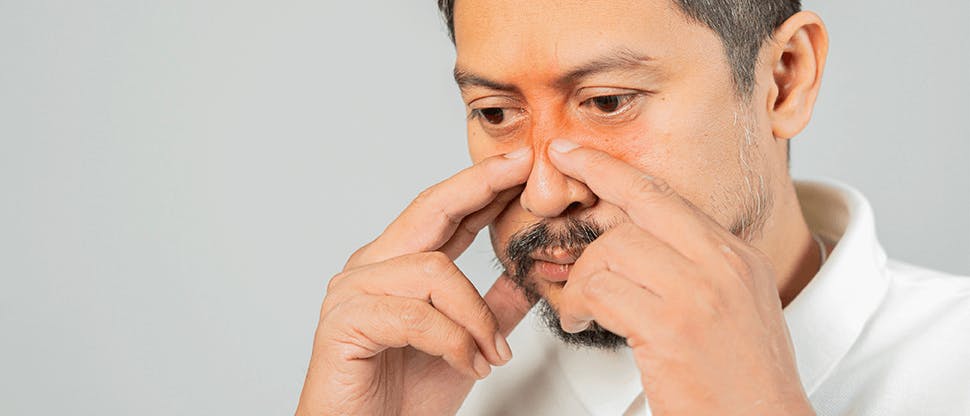 A man rubs the bridge of his nose with his forefingers as a result of sinus pressure.