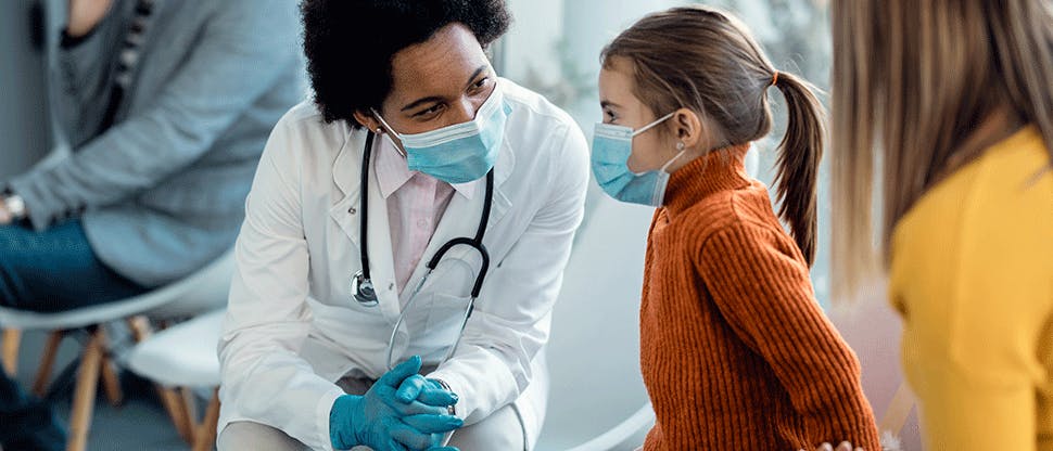 Masked doctor talks with young patient