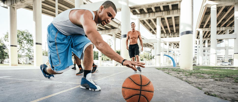 Man reaching for basketball while playing a pick-up game with a friend 
