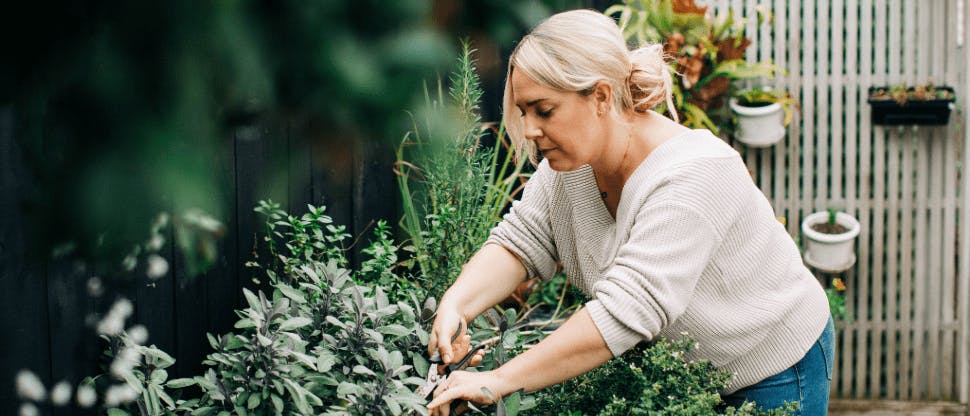Woman leaning over to prune plants in her garden 