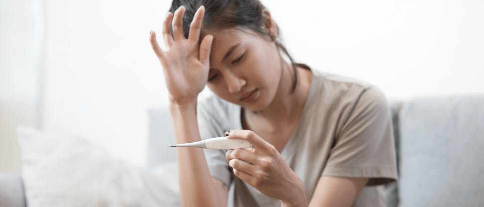 Woman with fever holding thermometer