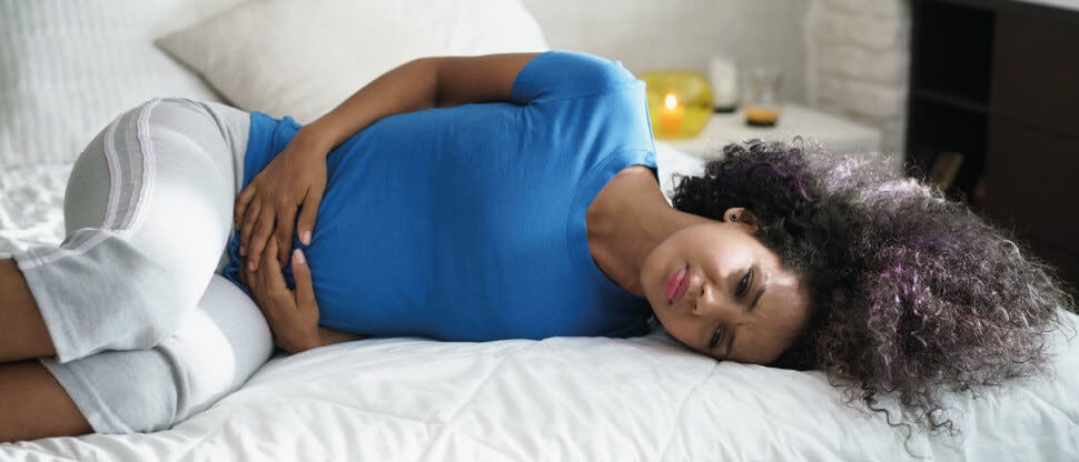 Young woman laying on bed experiencing menstrual pain