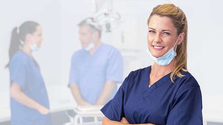 Smiling dental hygienist in scrubs with coleagues in the background