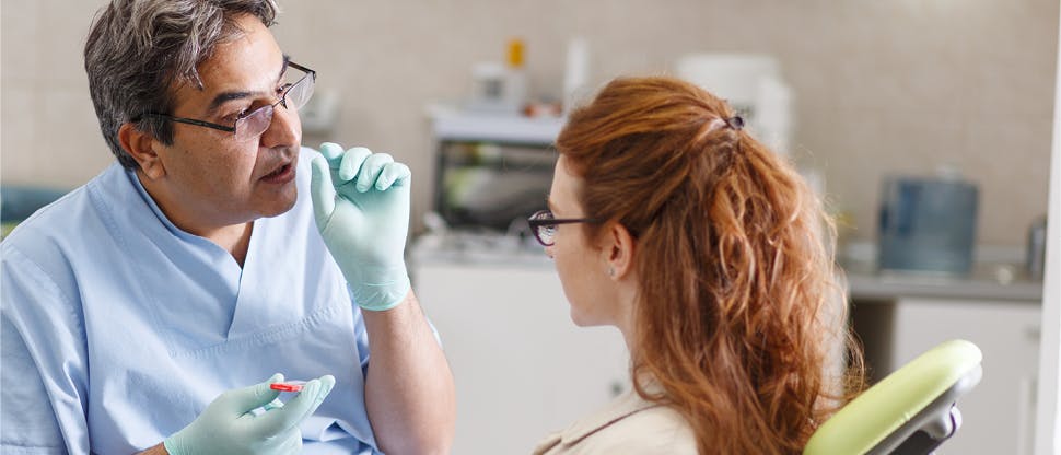 Male orthodontist with glasses conversing with female patient as she sits in the appointment chair