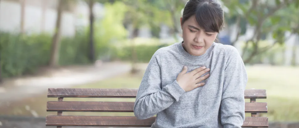 Woman sitting on a park bench holding her chest, indicating GERD