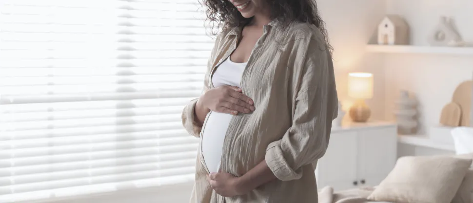 Expectant mother standing in a bright, calming room, gently holding her baby bump while wearing a soft, neutral-toned outfit