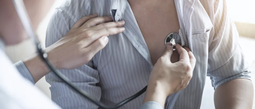 A healthcare professional uses a stethoscope to listen to the chest of a person wearing a striped shirt during a medical examination