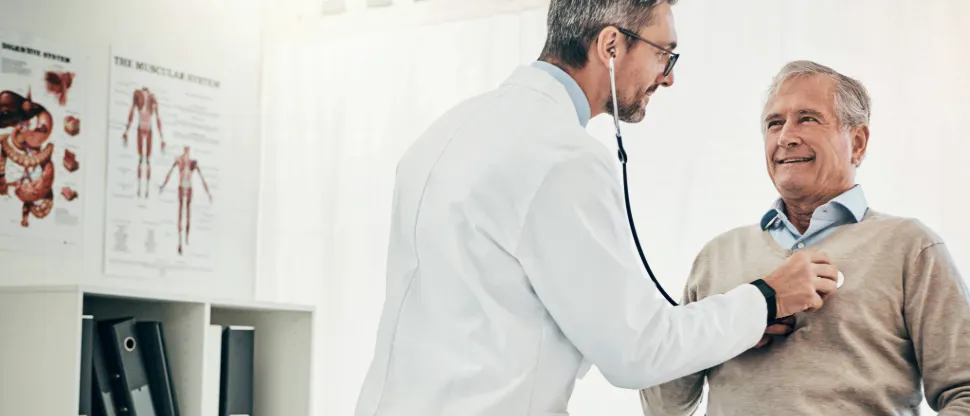 Healthcare professional using a stethoscope to examine a seated patient in a medical exam room