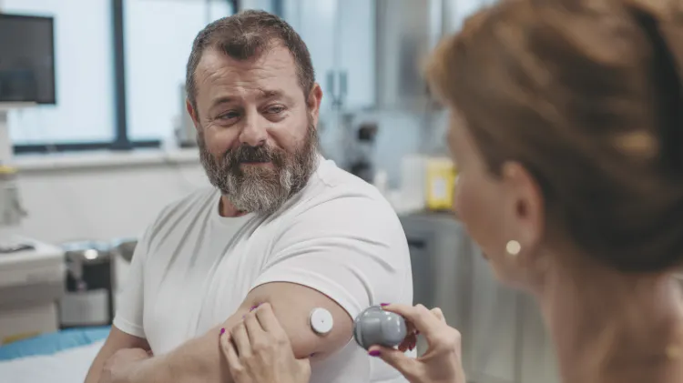 Healthcare professional applying a continuous glucose monitor to a patient’s upper arm in a clinical setting