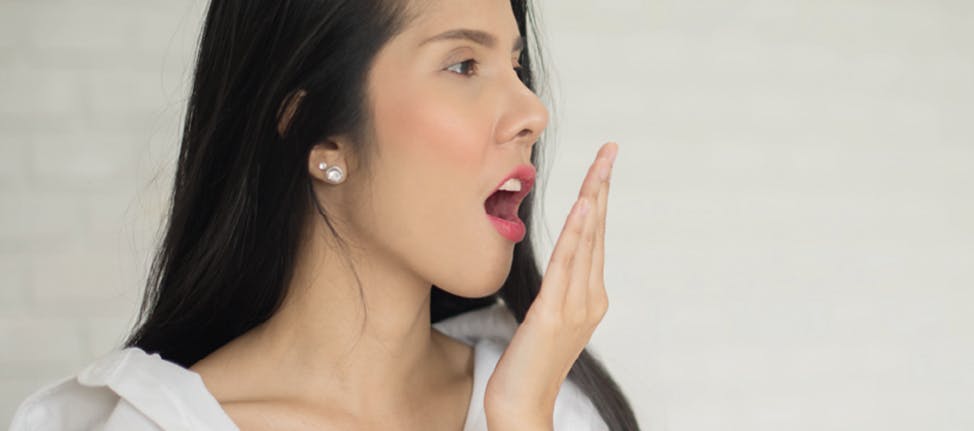 Young woman in a white shirt testing her breath with her hand