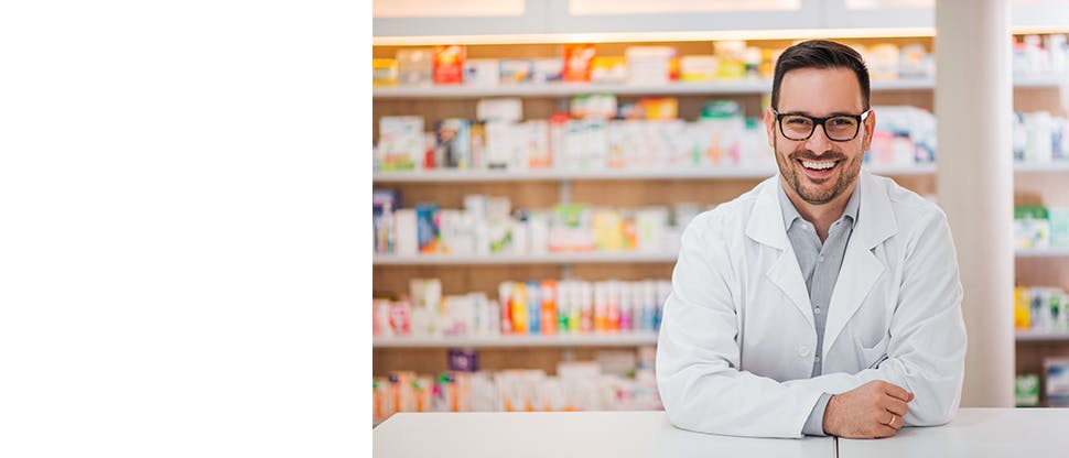 Smiling doctor wearing white coat standing in front of medicine shelf