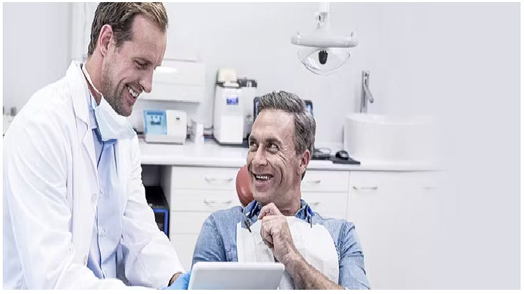 Patient in a dental chair smiles at a dentist as he is shown something on the dentist’s tablet