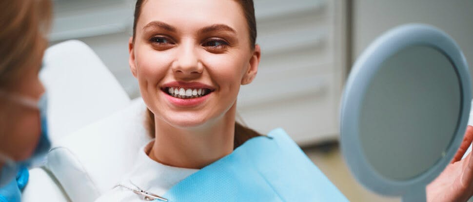 Dentist using tools in patient’s mouth while patient holds up a mirror to see their teeth