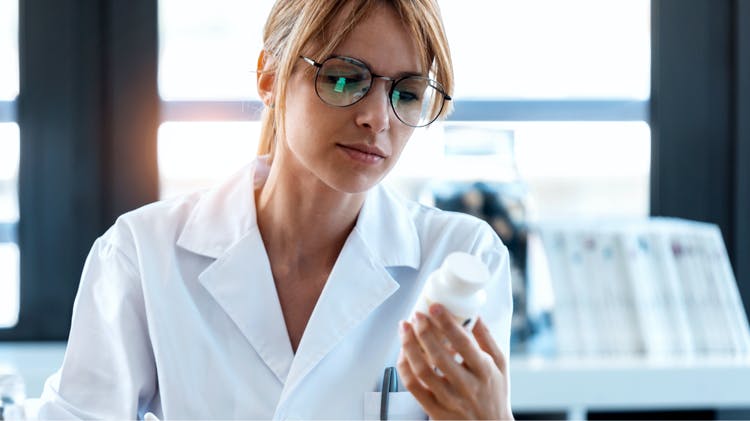 A young female scientist wearing glasses inspecting a medication bottle