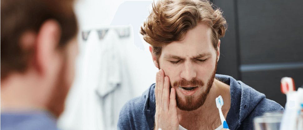 Hombre con hipersensibilidad dental cepillándose los dientes