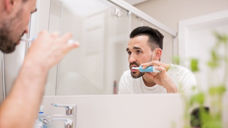 Un hombre cepillándose los dientes con una crema dental diaria con flúor como Parodontax