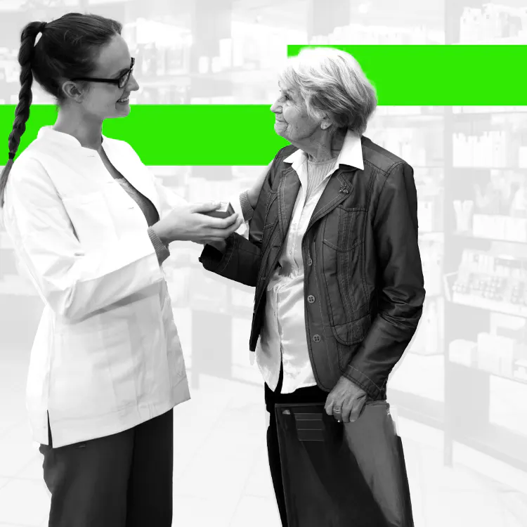 Una joven farmacéutica hablando con una paciente mayor mientras le toma la mano 