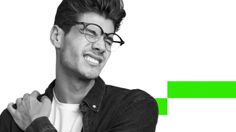 Joven con gafas se agarra el hombro y hace una mueca de dolor 