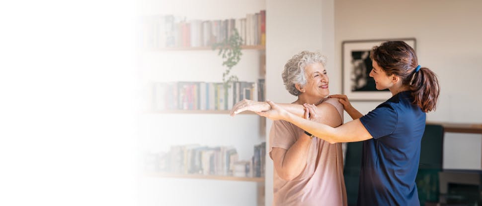 Mujer mayor feliz haciendo ejercicio en casa con fisioterapeuta.