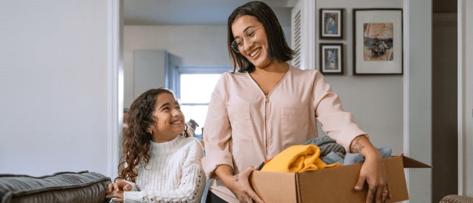 Mamá cargando caja e hija sonriendo