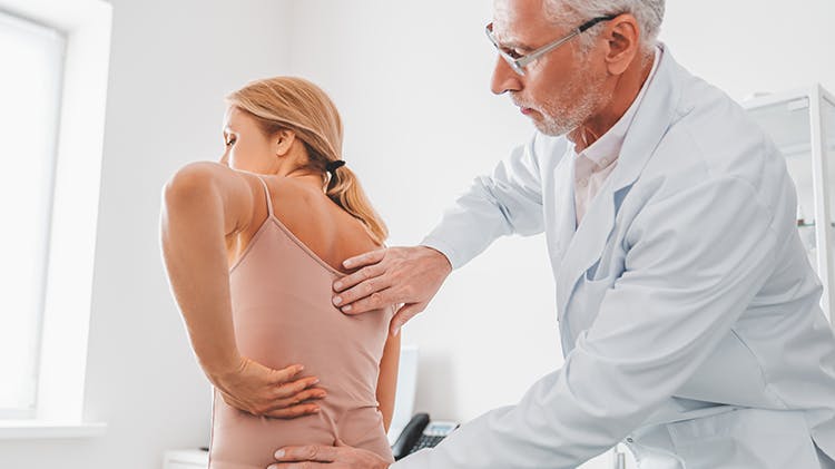 Image d’un médecin examinant la douleur dorsale d’une patiente.