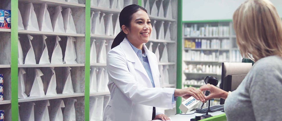 Pharmacienne à son comptoir, remettant un produit Sensodyne à une cliente