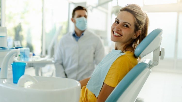 Une femme est assise sur un fauteuil dentaire et regarde vers l'extérieur avec un large sourire.