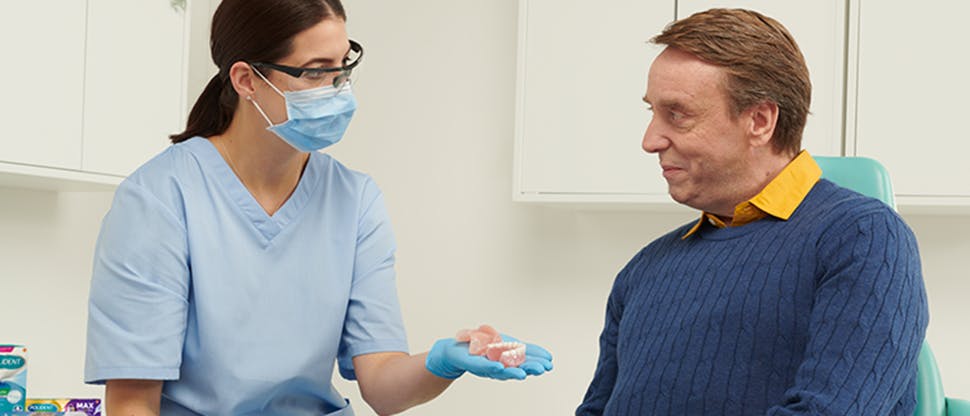 Dentiste tenant un ensemble de prothèses dentaires et discutant avec un patient