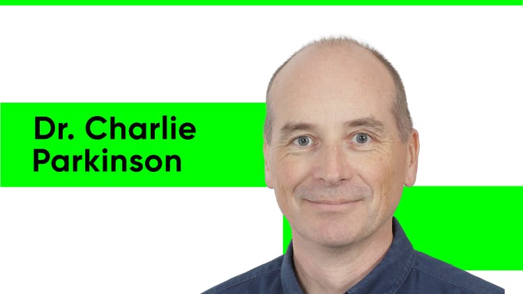 Portrait du Dr Charlie Parkinson, un homme aux cheveux noirs courts et aux sourcils foncés. Il porte une chemise noire