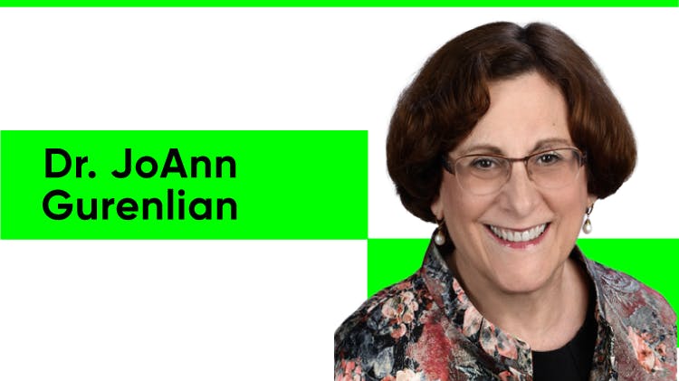 Dr. JoAnn Gurenlian arcképe, egy fehér nő rövid, bob fazonú barna hajjal. Szemüveget, gyöngy fülbevalót és virágmintás inget visel fekete felső fölött