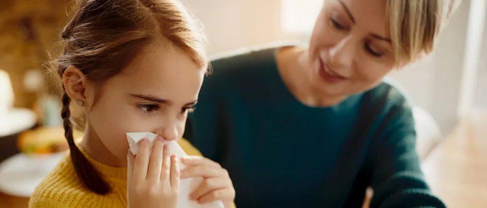 Egy fiatal anya a gyermeke homlokára teszi a kezét, miközben a gyermek zsebkendőt tart az orrához