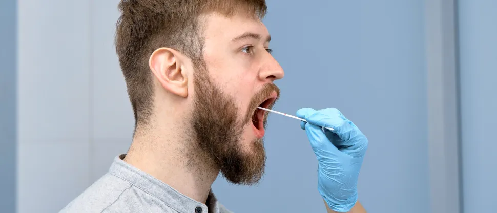 Egy fiatal férfitól szájüregi mintát vesz egy egészségügyi szakember, aki gumikesztyűt visel